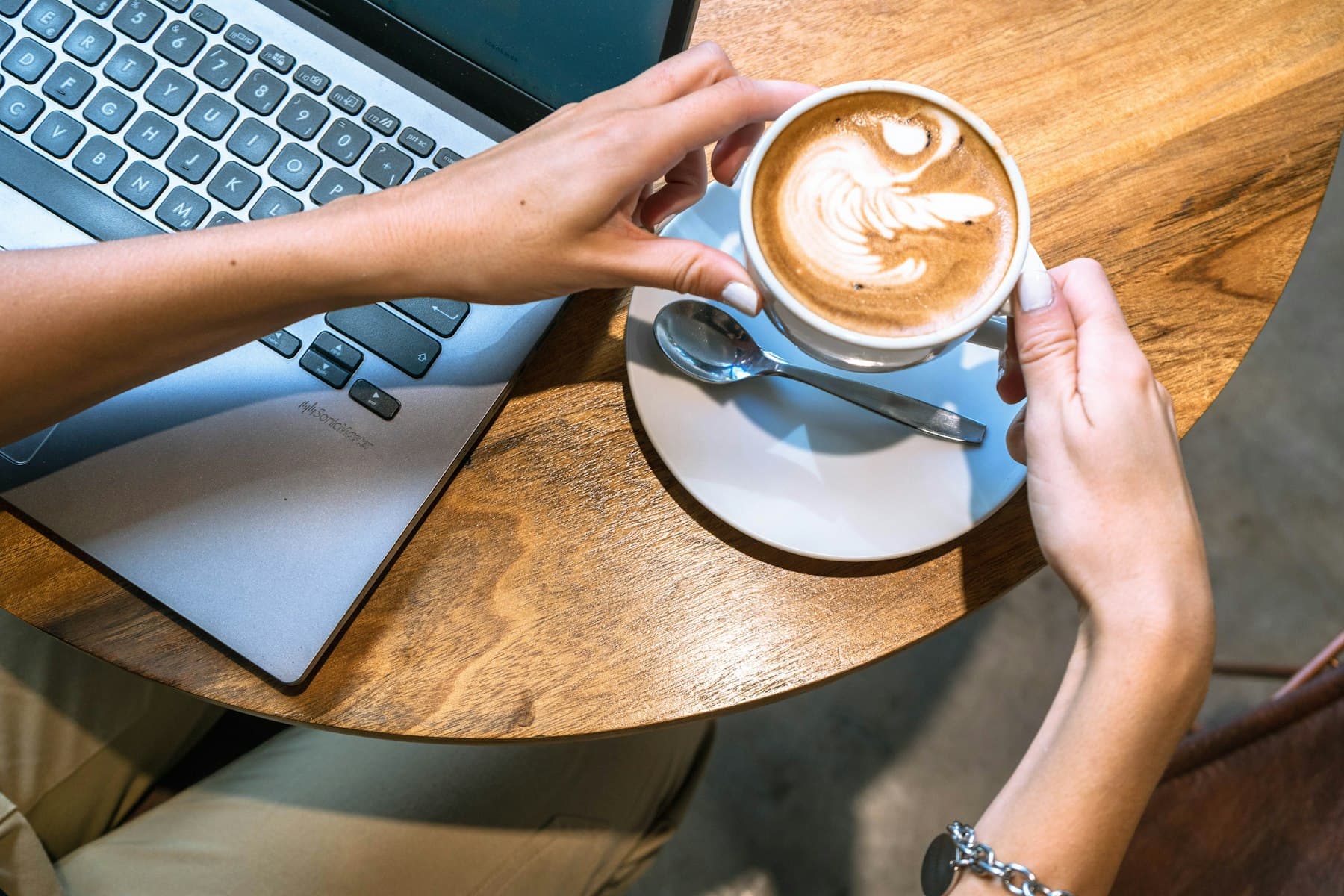Hands holding a latte next to a laptop